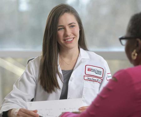 A Fox Chase doctor sits at a table across from a patient, holding a paper in their hands and smiling.