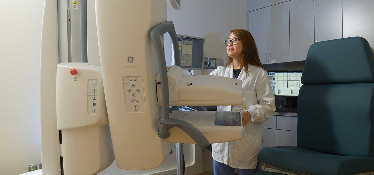 A photo of a medical professional looking at a mammogram machine.