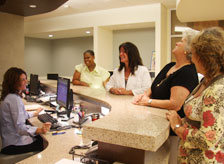 A photograph of a medical reception desk with several smiling people standing around it.