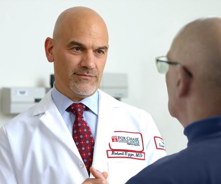 A photo looking over the shoulder of a patient in a medical chair, to a Fox Chase doctor standing nearby.