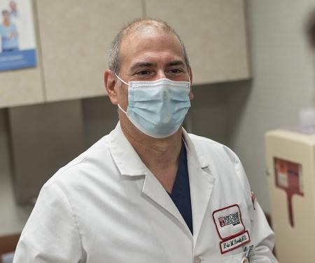 A photo looking over the shoulder of a patient as a masked Fox Chase doctor looks at them, both standing in a medical room.