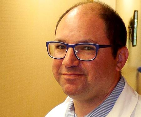 A closeup photo of Dr. Jeffrey M. Farma, MD, FACS, standing by a wall and smiling at the camera.