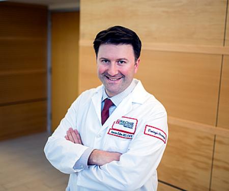 A Fox Chase doctor stands in front of a wooden wall, smiling at the camera.