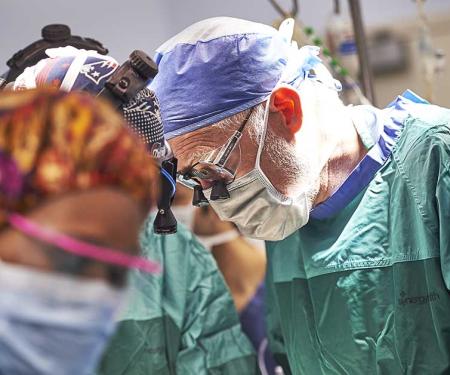 A group of doctors in full surgical gear all look down at the same thing, what they're doing obscured from view.